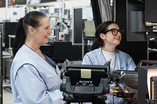 Two women in industrial environment smiling and looking at equipment